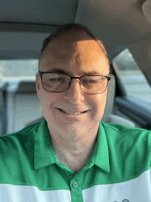 a man wearing glasses and a green shirt is smiling in a car