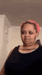 a woman with pink hair is wearing a black tank top and making a funny face .