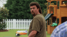 a man with a mullet and a beard is standing in front of a playground