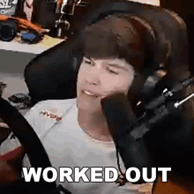 a man wearing headphones is sitting in front of a microphone with the words `` worked out '' above him .