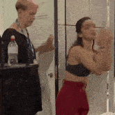 a woman in a black bra and red shorts is standing in a locker room .