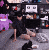 a man is sitting on the floor next to a cat and a purple stuffed animal .