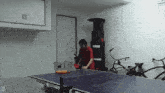 a man is playing ping pong in a garage with the letter d below him