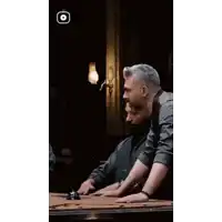 two men are sitting at a pool table in a dark room talking to each other .
