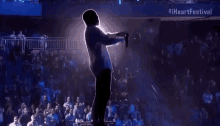 a man is singing into a microphone on a stage in front of a crowd of people .