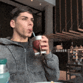 a man in a grey jacket drinking from a cup with a straw