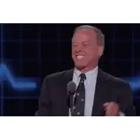 a man in a suit and tie is laughing while standing in front of a microphone .
