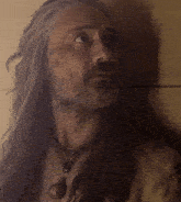 a man with long hair and a beard has a necklace with a bell on it