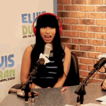 a woman wearing headphones is talking into a microphone in front of a wall that says elvis