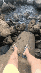 a person wearing flip flops is standing on a rock near a river