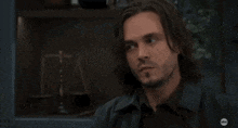a man with long hair and a beard is sitting in front of a shelf with scales of justice on it .