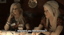 two blonde women are sitting at a table and one says " wouldn t you like to know "