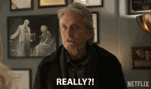 a man with a beard says really in front of a wall of framed pictures