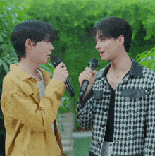 two young men singing into microphones in front of a green background