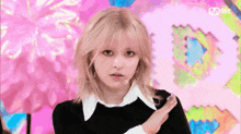 a woman with blonde hair and a white collar is standing in front of a pink and blue background .