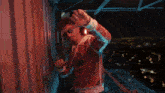 a man wearing sunglasses and a red hoodie is standing on a balcony
