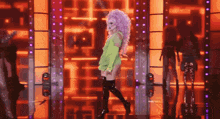 a drag queen with purple hair and thigh high boots is dancing on stage .