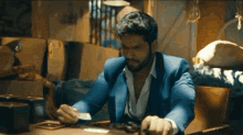 a man in a blue suit is sitting at a table counting cards