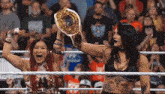 two women in a wrestling ring one holding a championship belt and the other screaming
