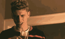 a young man in a black and red striped shirt is holding a glass