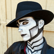 a man with face paint and a black hat is standing in front of a wooden wall