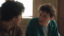two young men are sitting at a table talking to each other