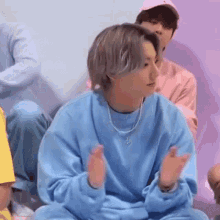 a person wearing a blue sweatshirt and a necklace is sitting on the floor with their hands in the air .