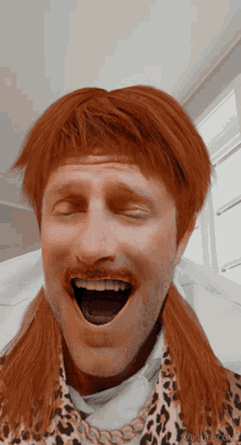 a man with red hair and a leopard print shirt laughs with his mouth open