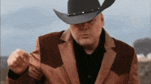 a man wearing a cowboy hat and a brown jacket is making a fist