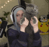 a woman wearing headphones is holding a cat in her hands