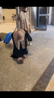 a woman wearing a mask is walking with a blue suitcase