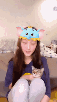 a woman wearing an elephant headband holds a cat in her lap