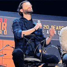 a man sitting in a chair with a microphone in front of a sign that says ' 20 years '