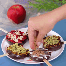 a person is adding nuts to a chocolate donut on a white plate