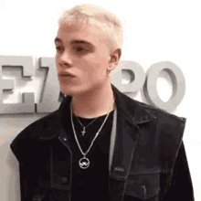 a young man wearing a denim jacket and a cross necklace