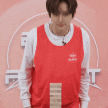 a man wearing a red shirt that says boys planet is playing jenga