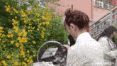 a woman stands in front of a bush with yellow flowers and the word university on the bottom right