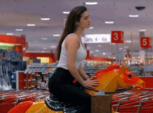 a woman in a white tank top is riding a rocking horse in front of a sign that says girls 4 6x