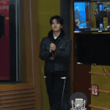a man in a black jacket stands in front of a microphone and applauds