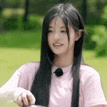 a girl with long black hair is wearing a pink shirt and holding a spoon .