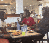 a man in a red t-shirt with the letter t on it sits at a table