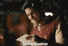 a man in a red vest is holding a piece of paper with the name mikelvelayudham on it