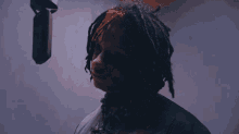 a person with dreadlocks stands in front of a microphone with a purple background