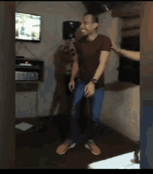 a man is dancing in a room with a tv on the wall behind him