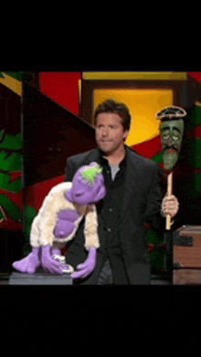 a man in a suit is holding a purple puppet in his hands