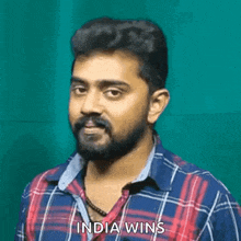 a man with a beard and mustache is wearing a plaid shirt and saying `` india wins '' .