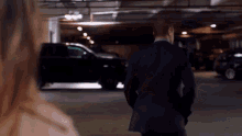 a man in a suit and a woman in a trench coat are standing in a parking garage .