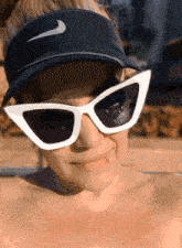 a woman wearing sunglasses and a nike visor smiles for the camera