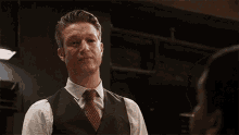 a man in a vest and tie looks at another man with his eyes closed