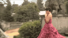 a woman in a pink dress is standing in front of a statue of a lion ..